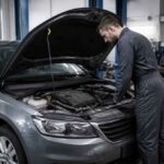 Mechanik w warsztacie sprawdza silnik szarego samochodu z otwartą maską