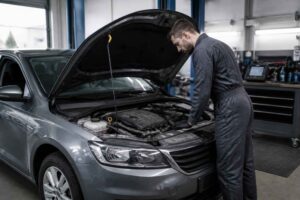 Mechanik w warsztacie sprawdza silnik szarego samochodu z otwartą maską